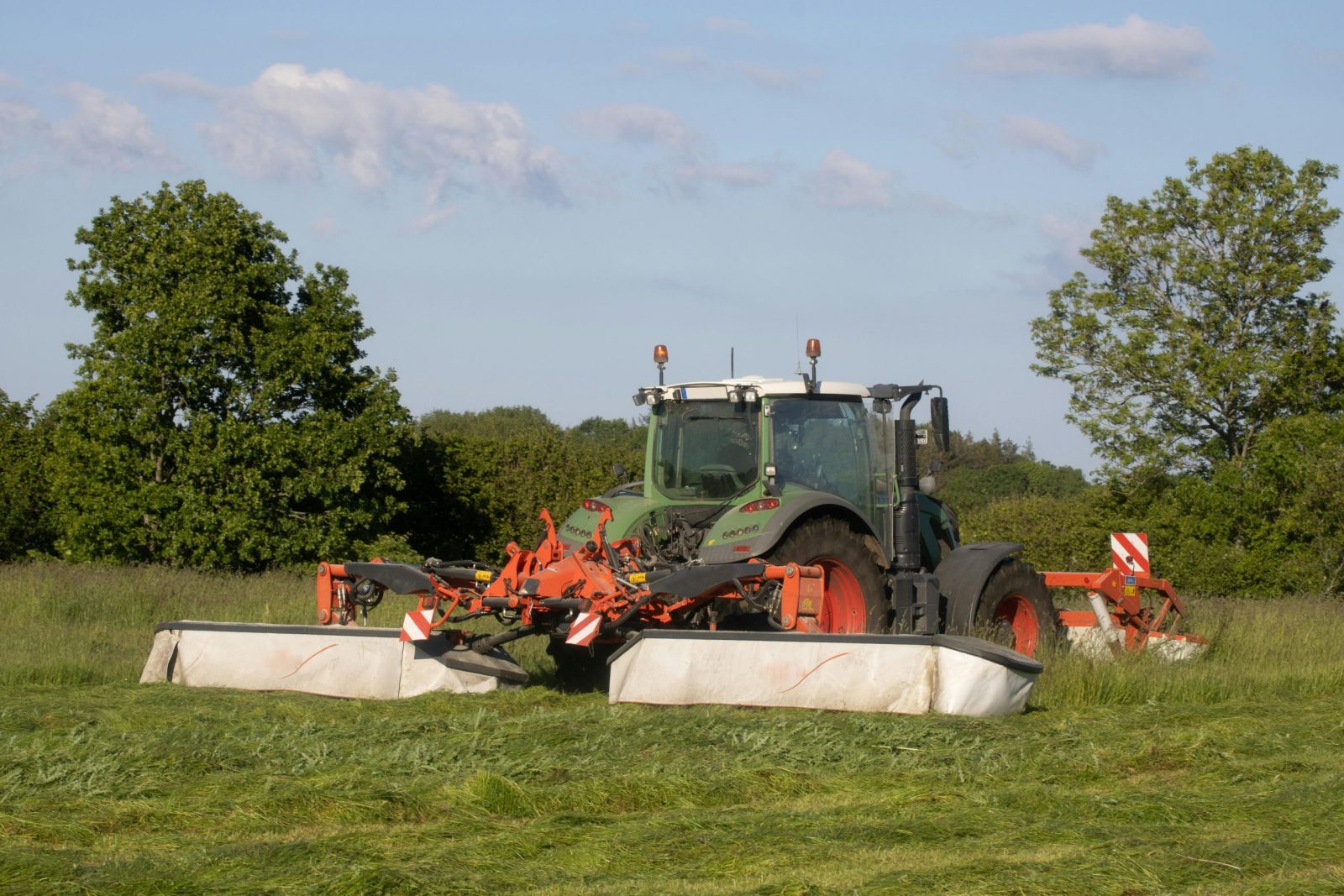 A powerful modern tractor mowing fields in a lush, sunny countryside, showcasing agricultural machinery at work.